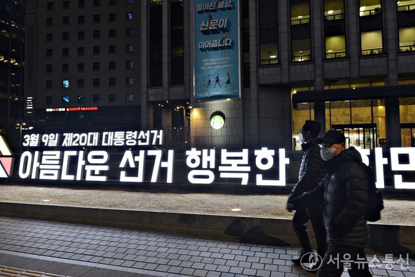 제 20대 대통령선거 D데이가 열렸다. 이번 선거는 전국 1만4464개 투표소에서 오전 6시부터 오후6시까지 실시된다고 중앙선관위가 밝혔다. 단, 확진자 격리자 투표는 오후6시 이후 오후 7시30분까지 할수있다. 8일 저녁 서울 시청 앞 프레스센터 앞에 설치된 20대 대통령선거 플래카드 앞으로 행인들이 바쁘게 지나가고 있다. (사진 = 이민희 기자)   